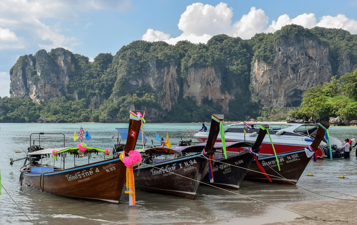 Long-tail boats at Railay West beneath forested limestone cliffs in Krabi